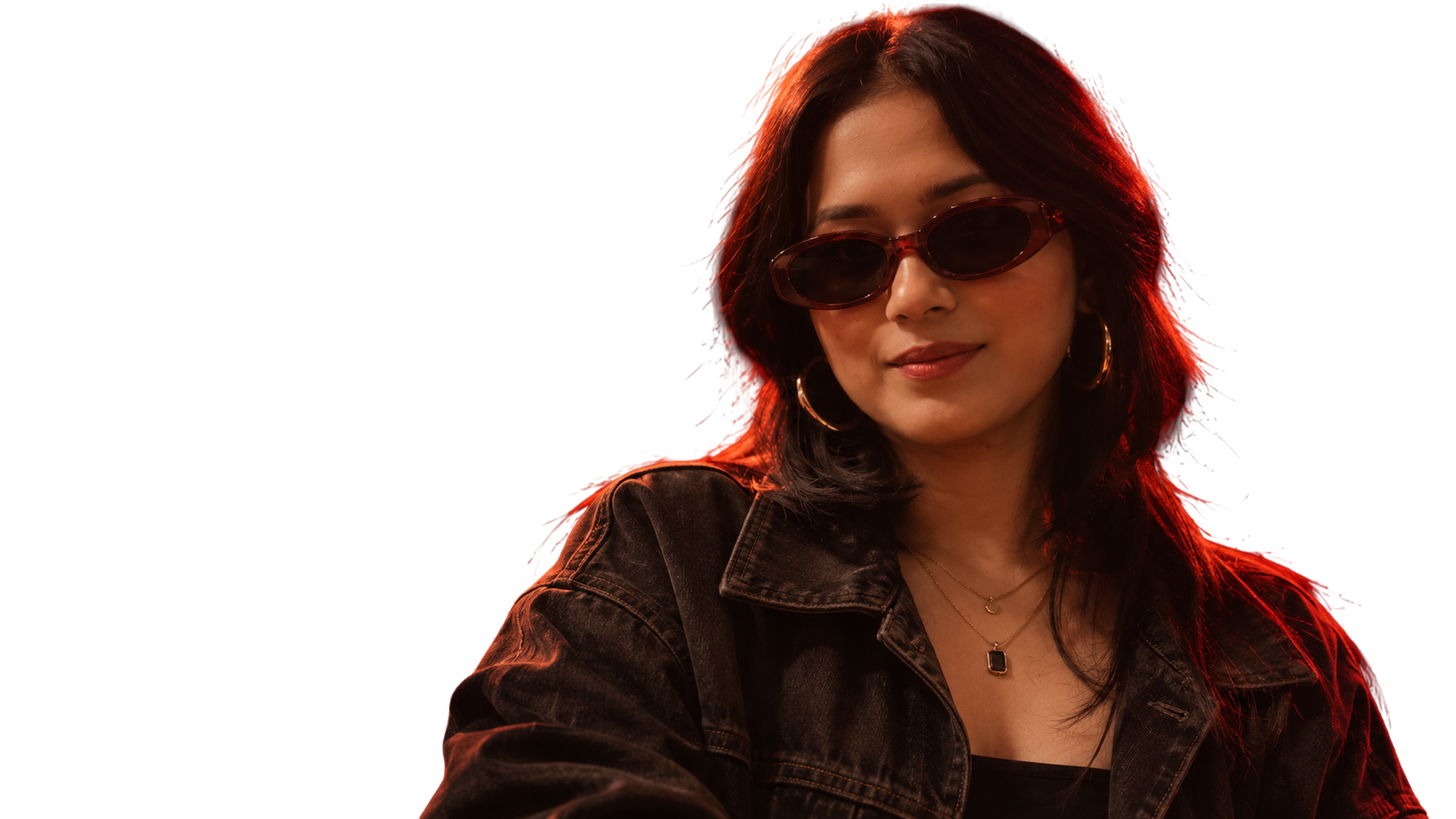Sreyasi in dark oval sunglasses, gold hoop earrings and a black denim jacket, with a slight smile, her hair rim-lit in red.